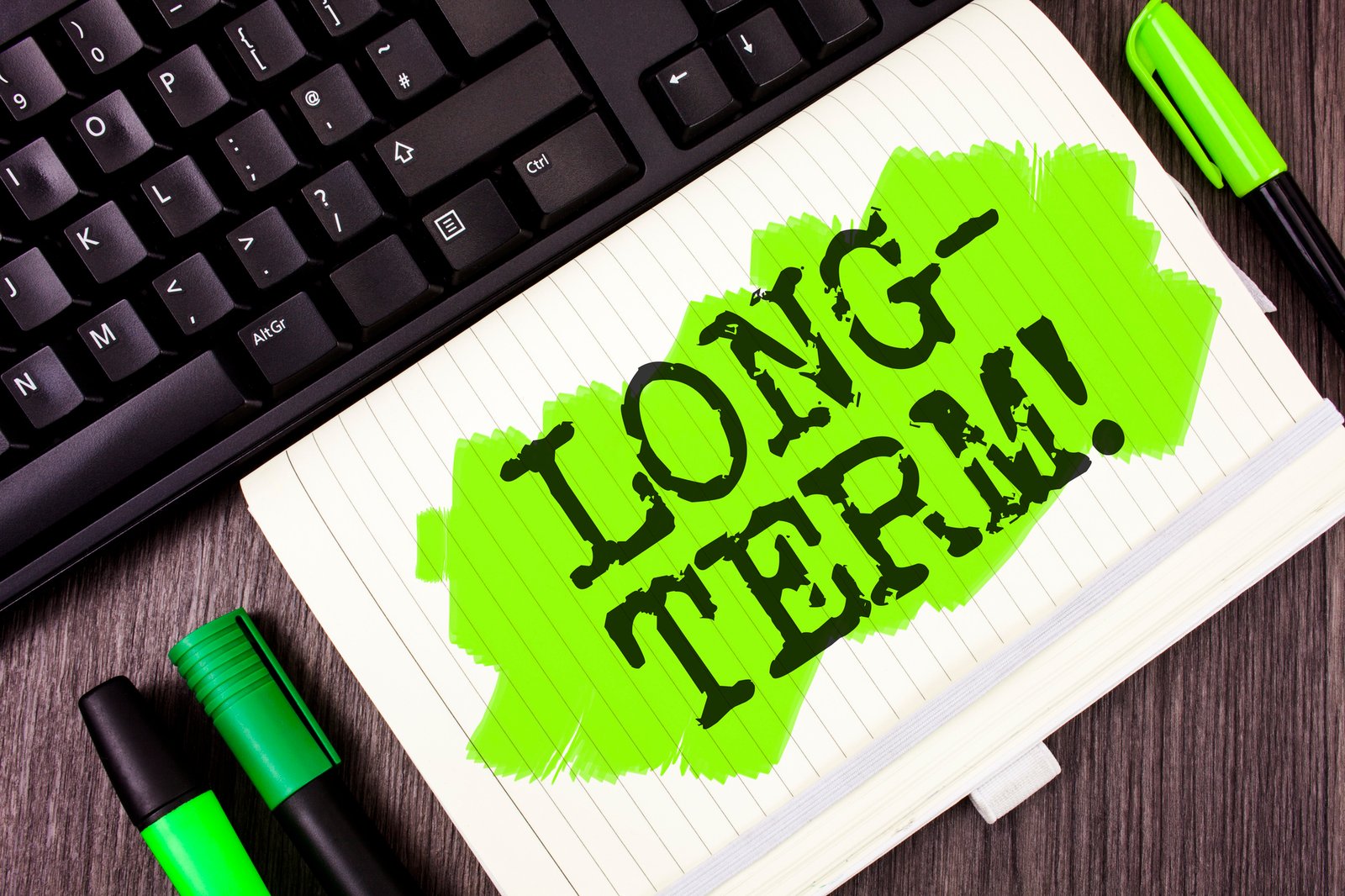 handwriting text writing long term motivational call. concept meaning occurring over large period of time future plans written on painted notebook book on wooden background marker and keyboard