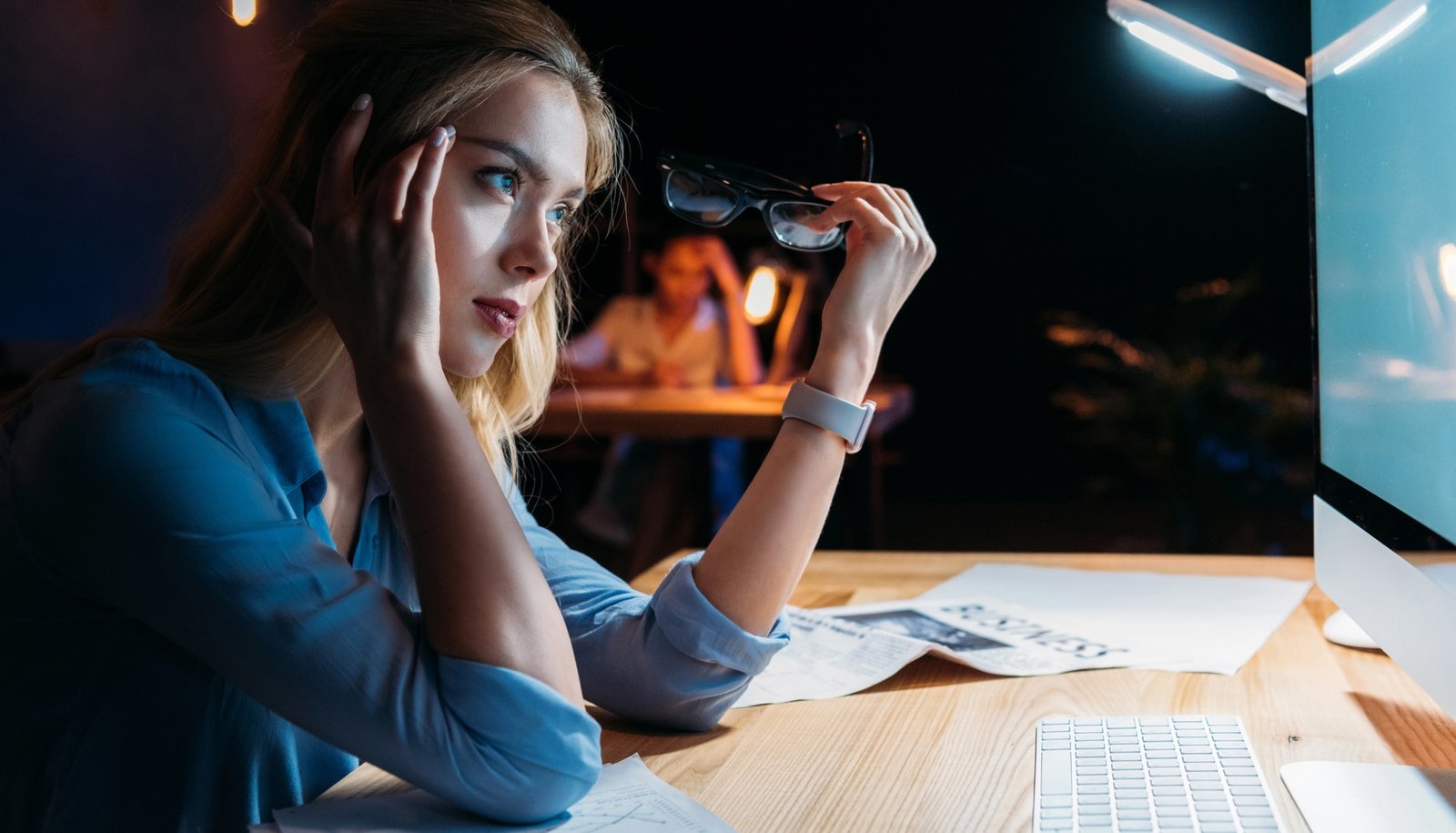 women working overtime, leaning over desk at work, at night. looking into computer 